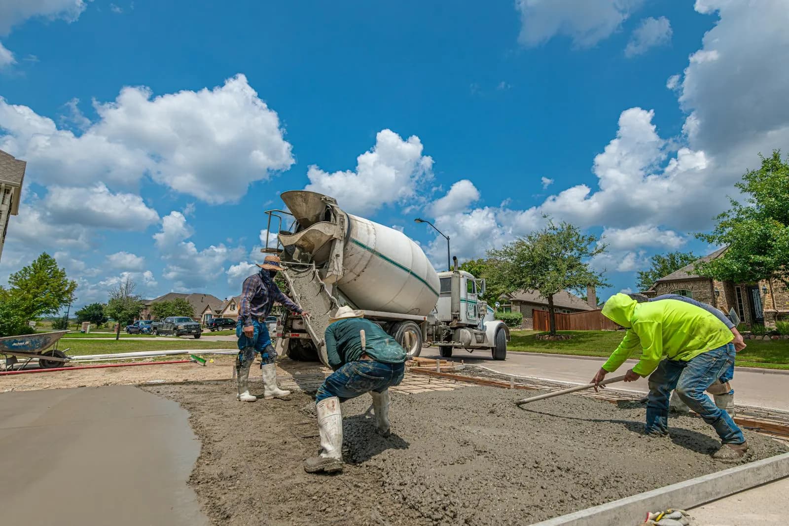 Crew laying a residential concrete driveway under bright daylight.